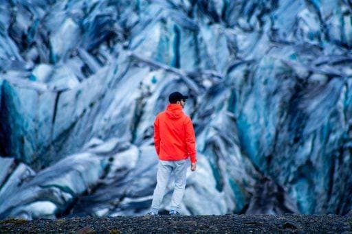 Creative Highlights Symbolfotos A man in a bright orange jacket stands in front of a striking blue glacier, showcasing a blend of human and natural beauty. 26299760 ,model released, Symbolfoto RECORD DATE NOT STATED