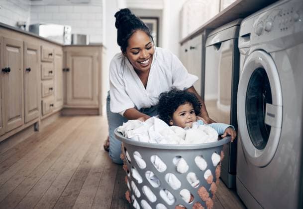 Creative Highlights Symbolfotos Mother, baby and helping with laundry in home, multitasking and chores responsibility. Mama, infant daughter and housekeeping with child in kitchen, cleaning and loading clothes in washing machine. model released property released Copyright: xwww,peopleimages.comx