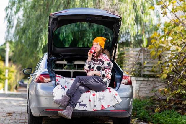 Woman in yellow beanie sitting with coffee in car trunk London, England, United Kingdom R_THNZ241217-1604247-01 ,model released, Symbolfoto
