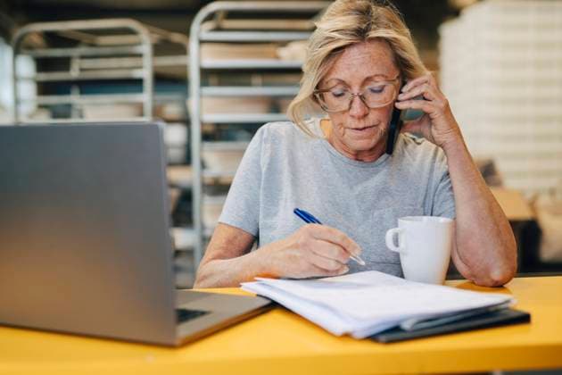 Senior female baker talking on smart phone while preparing notes at bakery Sweden, Stockholm, model released, property released Copyright: xMaskotx , MA114882 MA114882