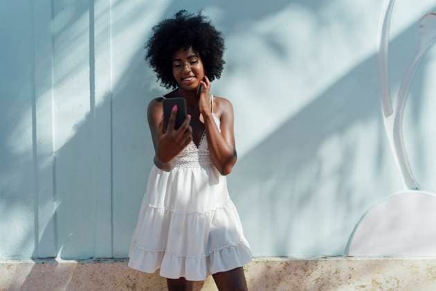 Creative Highlights Symbolbilder Smiling young woman wearing white dress looking at cell phone at a wall model released, Symbolfoto, BOYF00815