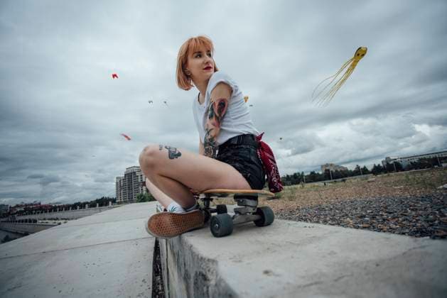 Creative Highlights Symbolbilder Young woman sitting on a concrete wall on carver skateboard with kite in background model released, Symbolfoto, VPIF00996