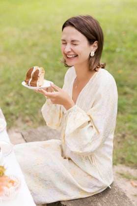 Creative Highlights Symbolbilder Cheerful woman with closed eyes holding cake in plate at garden party model released, Symbolfoto, ONAF01068