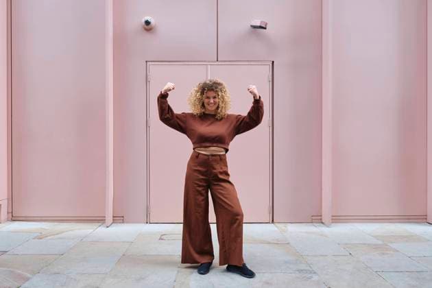 Young woman with curly hair flexing muscles in front of pink wall model released, Symbolfoto, ASGF05813
