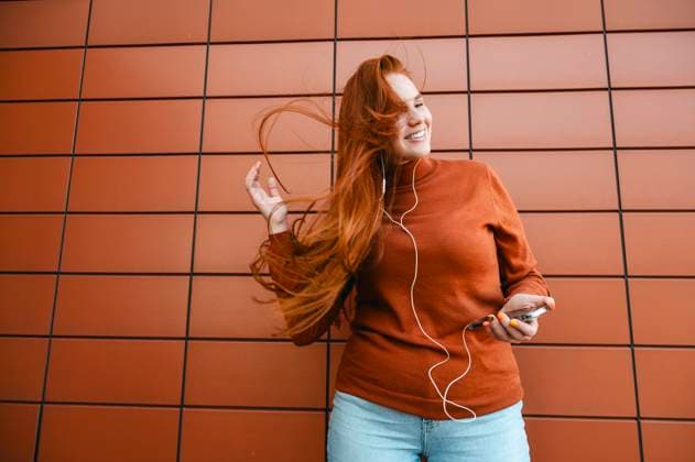 Creative Highlights Symbolbilder Happy redhead woman with long hair listening to music through in-ear headphones near brown wall model released, Symbolfoto, ALKF01403