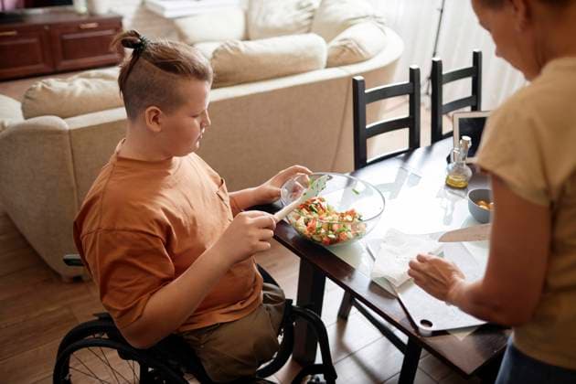 Boy sitting in wheelchair near mother cooking salad at home model released, Symbolfoto property released, KPEF00885