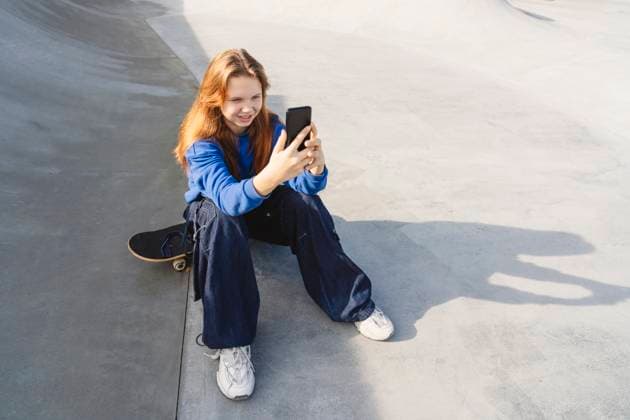 Creative Highlights Symbolbilder Smiling girl sitting on skateboard and using smart phone in park model released, Symbolfoto, IHF02193