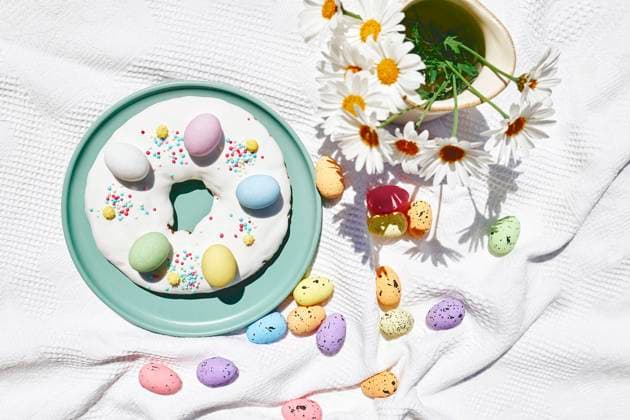 Easter doughnut decorated with colorful chocolate eggs near flowers on table, CATF00554
