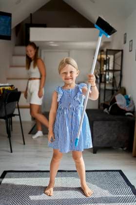 IMAGO Creative, Frühling, Frühjahrsputz Smiling girl standing with broom in living room at home model released, Symbolfoto property released, ANNF01059