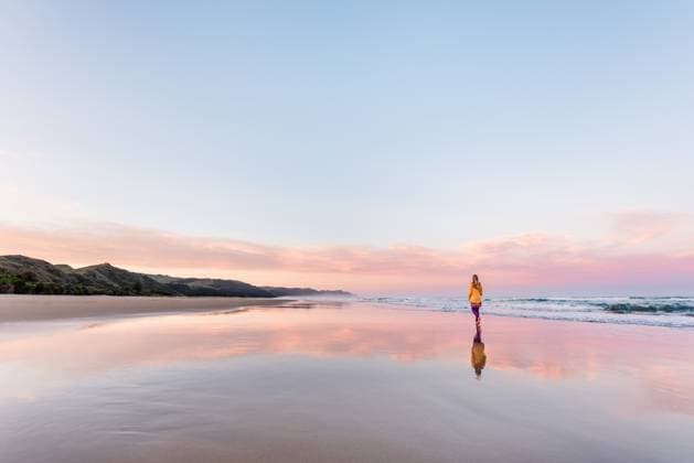 Creative Highlights Symbolbilder Young woman walking on beautiful beach with pink clouds Ocean Beach, Hawke s Bay, New Zealand CR_JUCR241229-1616656-01 ,model released, Symbolfoto