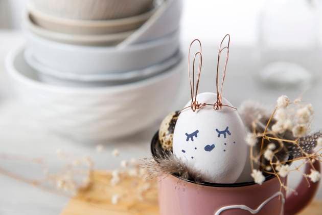 Easter concept. A white egg with copper wire ears and a painted rabbit sleeping face in a cup. Partridge eggs and feathers. , 45193442.jpg, ear, banner, holiday, table scape, symbol, decor, tableware, copy space, invitation, flat lay, breakfast, food, festive, table, background, traditional, bunny, rabbit, white, spring, setting, easter, happy, dinner, top view, serving, concept, celebration, decoration, egg, lunch, flower, place, linen, table setting, card, branch, glass, hare, plant, holder, handmade, craft, dreamy, bowl, plate, cup, filler, pink, heart RECORD DATE NOT STATED