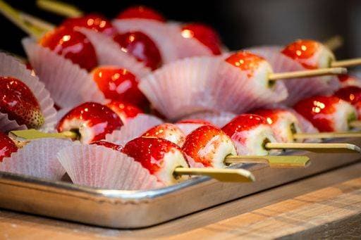 Close-up of candied strawberries on skewers arranged in paper cups on a tray, showcasing vibrant red colors and glossy texture. 27949217 RECORD DATE NOT STATED