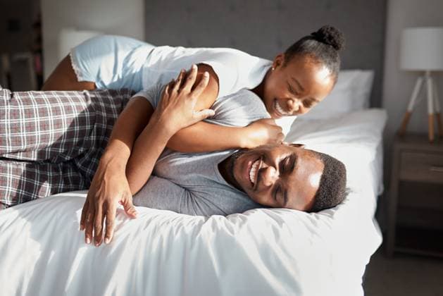 Creative Highlights Symbolbilder Black couple, smile and play on bed with love, affection and teasing game in home. Happy man, girlfriend and excited in bedroom for bonding, relationship development and weekend relax in apartment. model released property released Copyright: xwww.peopleimages.comx