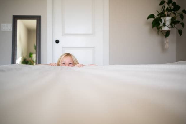 Creative Highlights Symbolbilder Blonde Girl Playfully Peeking Over Edge of Bed in Cozy Bedroom Syracuse, Utah, United States R_WMWJ250102-1613634-01 ,model released, Symbolfoto