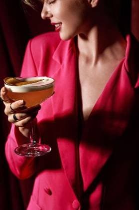 Creative Highlights Symbolbilder Elegant woman in pink blazer holding a cocktail in a dimly lit setting, showcasing modern style and sophistication. 28318476 ,model released, Symbolfoto RECORD DATE NOT STATED