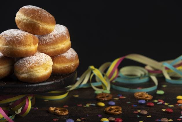 Berliner, Krapfen mit Puderzucker stapeln sich vor einem dunklen Hintergrund neben Konfetti und Brezeln Berliners, doughnuts with icing sugar are piled up against a dark background next to confetti and pretzels Copyright: imageBROKER LucasxSeebacher ibxlse12103523.jpg