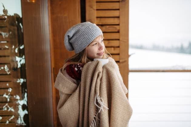 Smilng teen girl bundled in thick blanket holding cup of hot tea standing on balcony during winter day. Smiling teen girl bundled in thick blanket holding cup of hot tea standing on balcony during cold winter day. model released