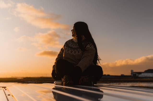 Creative Highlights Symbolbilder Colombian woman sitting calmly on a camper roof, gazing towards a picturesque Iceland sunset, embodying peace and solitude. Model Released Centric_ID25620_739899_015 Copyright: xCentricx RECORD DATE NOT STATED