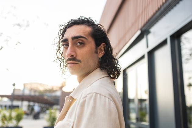 Creative Highlights Symbolbilder A stylish young man with curly hair and a mustache stands confidently outdoors, backlit by the setting sun He wears casual attire, reflecting a modern urban lifestyle Model Released DavidMunoz_ID25758_743994_027 Copyright: xDavidxMunozx
