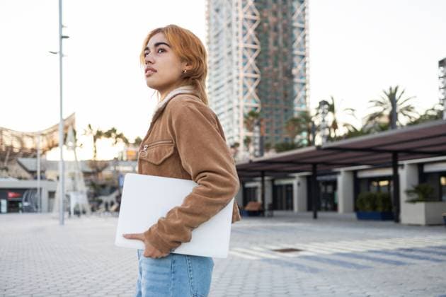 Creative Highlights Symbolbilder A mixed race woman with a focused expression holds a laptop while standing in an urban area, showcasing modern fashion and architecture She wears a suede jacket and jeans Model Released DavidMunoz_ID25936_748820_025 Copyright: xDavidxMunozx
