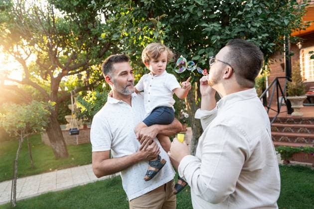A joyful gay couple spends a sunny afternoon outdoors with their young son, engaging in playful activities, surrounded by lush greenery in their backyard. Model Released ManuelRuiz_ID25867_747197_044 Copyright: xManuelxRuizx