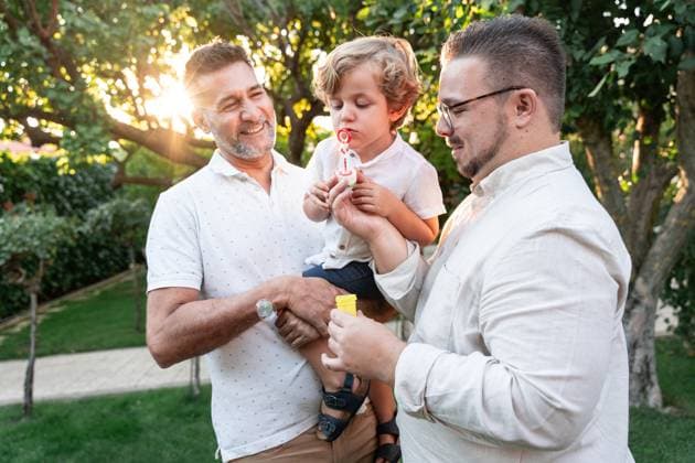A joyful gay couple spends quality time with their son in a sunlit garden, enjoying a playful moment with bubbles. Family love and happiness in an outdoor setting. Model Released ManuelRuiz_ID25867_747205_052 Copyright: xManuelxRuizx