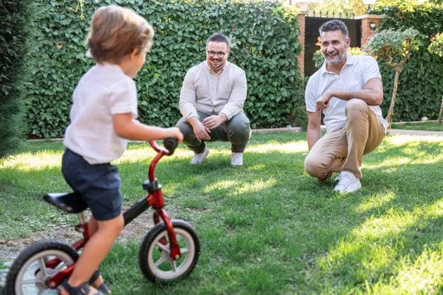 A joyful moment with a gay couple watching their son ride a bicycle in a lush garden. The scene reflects a loving family enjoying quality time together outdoors. Model Released ManuelRuiz_ID25867_747224_071 Copyright: xManuelxRuizx