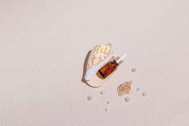 A skincare serum bottle surrounded by seashells and pearls on a soft pastel background The minimalistic composition conveys elegance and natural beauty Model Released MarinaMos_ID25391_734005_013 Copyright: xMarinaxMosx RECORD DATE NOT STATED