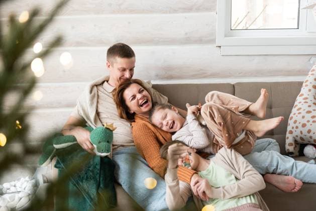 A joyful family celebrates Christmas in a cozy home setting. Two adults and two children, all laughing and cuddling on a sofa, are surrounded by Christmas decorations and soft lighting. Model Released Shapovalphoto_ID25696_741699_034 Copyright: xShapovalphotox