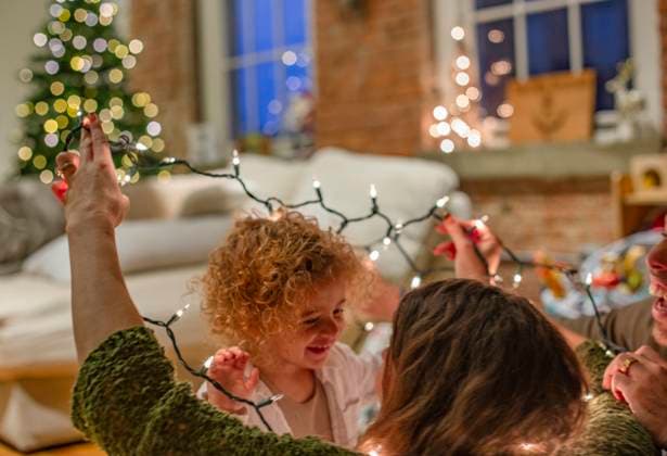 Joyful child with curly hair and an adult holding up Christmas lights in a festively decorated room, Ohio, USA Ohio USA arah00957 Copyright: xConnectxImagesx ,model released ,property released