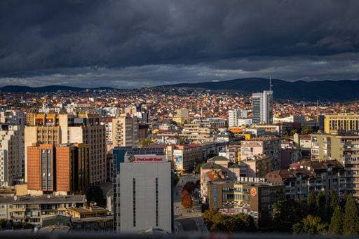 Aerial view of Pristina cityscape under dramatic cloudy sky, showcasing urban architecture and distant hills, Kosovo. 28523915