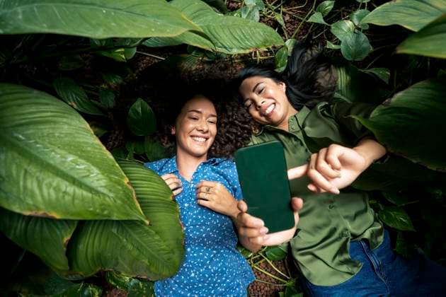 Smiling woman taking selfie on mobile phone with friend lying amidst plants model released, Symbolfoto property released, JOSEF22597