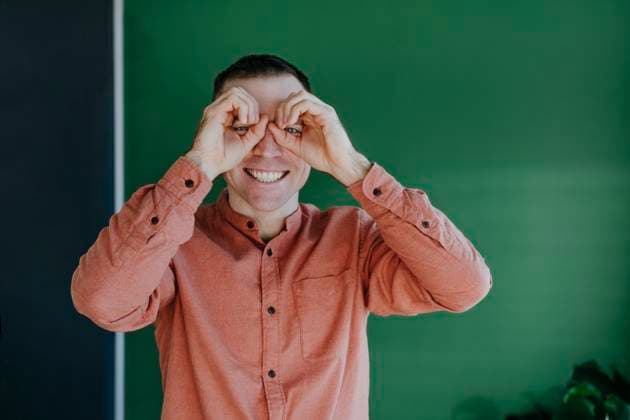 Playful man looking through finger binoculars in front of green wall model released, Symbolfoto property released, YTF01666