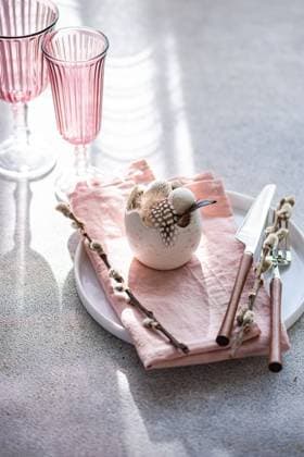 An elegant and festive Easter table setting in soft pastel hues. The focus is a decorative egg centerpiece surrounded by blooming willow twigs on a pink napkin. Nearby, pink glassware adds a touch of sparkle. Model Released AnnaBogush_ID26004_750165_008 Copyright: xAnnaxBogushx RECORD DATE NOT STATED