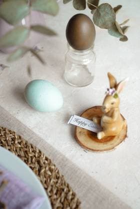 From above, an Easter table is set with naturally dyed eggs in soft pastel shades, accompanied by an ornamental bunny figure holding a Happy Easter sign Model Released CamilaMacedo_ID26016_750691_005 Copyright: xCamilaxMacedox RECORD DATE NOT STATED