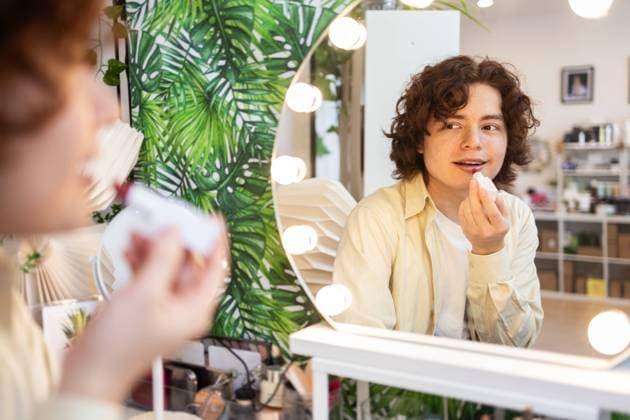 IMAGO Creative, Naturkosmetik A young man applies lipstick while looking into a mirror surrounded by lights in an organic beauty shop The eco-friendly store features natural cosmetics and lush green decor Model Released DavidMunoz_ID26067_751986_050 Copyright: xDavidxMunozx