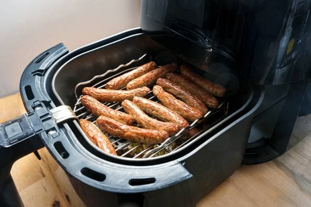 Kleine Würstchen aus Schweinefleisch, in Deutschland Nürnberger Rostbratwurst genannt, in einer Heißluftfritteuse auf einem Rost gebraten, schnelle Methode zum Braten von Lebensmitteln mit weniger Öl, aber mit faltiger Haut, ausgewählter Schwerpunkt Small pork sausages, in Germany called Nuremberg rostbratwurst, roasted in a hot air fryer on a rack, quick method of frying food with less oil but with wrinkled skin, selected focus, narrow depth of field Copyright: xZoonar.com MarenxWinterx 22695207