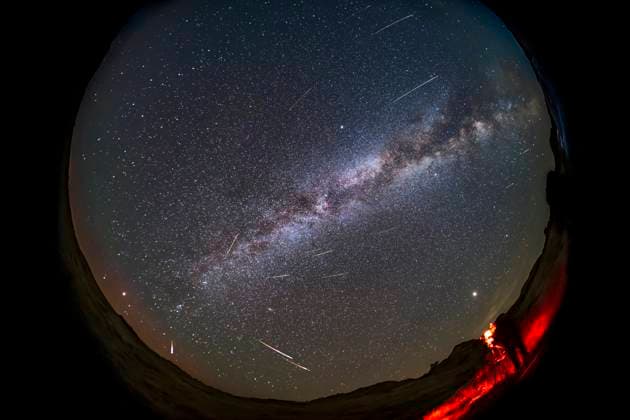 A selfie of astronomer setting up to photograph the 2021 Perseid meteor shower on August 12, 2021 at Dinosaur Provincial Park, Alberta, Canada, as one camera captures the scene looking east while I finish setting up another camera in the foreground. The radiant of the shower is obvious, in Perseus, at lower left in the northeast. The Milky Way stretches from northeast to southwest (top right). A dim red aurora is on the horizon to the northeast. Cygnus is overhead at centre. Jupiter is the bright object above me. The Big Dipper is at upper left low in the northwest. Model Released Copyright: AlanxDyer StocktrekxImages ADY201276S