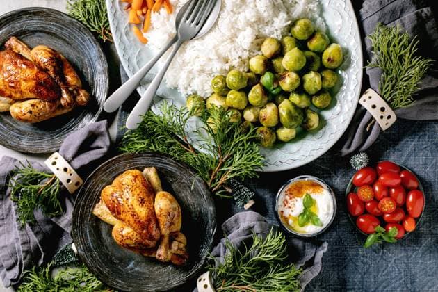 Weihnachtsessen mit gegrilltem Huhn, Reis und Gemüse Christmas dinner table with grilled mini chicken, rice and vegetables baked brussel sprouts, baby carrot in ceramic bowls, xmas decorations on blue linen tablecloth over grey background. Flat lay. Copyright: xZoonar.com NATASHAxBREENx 22744328