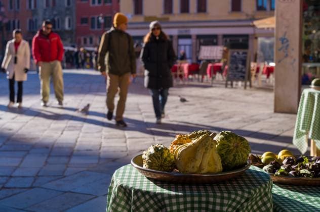 IMAGO Creative, Jahreszeit Herbst in der Stadt Auslage von Straßenmarktprodukten Fresh gourds, lemons, and artichokes displayed on a checkered tablecloth in a sunny outdoor market setting. Pedestrians walk by in the background. Copyright: xZoonar.com PeterxBuchacherx 22776646