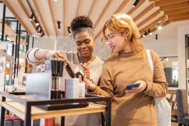 IMAGO Creative, Naturkosmetik Two women in a bright cosmetics store share a friendly interaction while exploring makeup products. The setting emphasizes modern design, natural light, and diverse beauty selections. Model Released DavidMunoz_ID26443_763057_059 Copyright: xDavidxMunozx