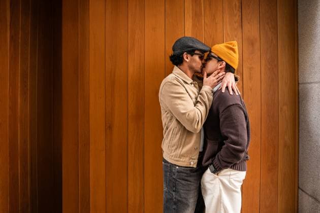 A loving Colombian gay couple shares a tender kiss while standing against a warm wooden wall. Their casual attire and intimate gesture highlight affectionate, everyday moments. Model Released ManuelRuiz_ID26426_762394_038 Copyright: xManuelxRuizx RECORD DATE NOT STATED
