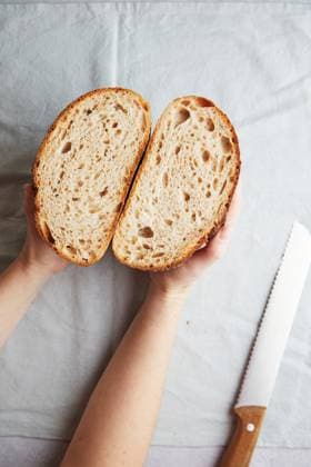 Top view of cropped unrecognizable person s hands holding fresh homemade sourdough bread halves, showcasing the airy texture and golden crust, accompanied by a bread knife on the side. Model Released TwoInspirations_ID26492_764451_008 Copyright: xTwoxInspirationsx RECORD DATE NOT STATED