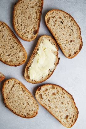 Top view of sliced fresh homemade sourdough bread with some slices generously spread with butter, set on a grey textured surface. Model Released TwoInspirations_ID26492_764459_013 Copyright: xTwoxInspirationsx RECORD DATE NOT STATED