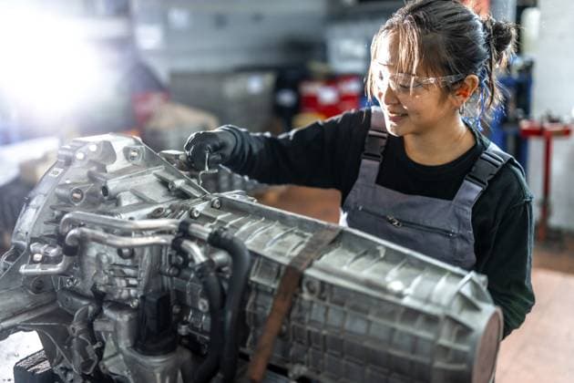 Asiatische Mechanikerin bei der sorgfältigen Arbeit an einem Fahrzeuggetriebe in einer professionellen Werkstatt, die ihr Können und ihre Erfahrung bei der Reparatur von Kraftfahrzeugen unter Beweis stellt Asian woman mechanic working diligently on a vehicle gearbox in a professional garage, showcasing skill and expertise in automotive repair Copyright: imageBROKER UnaixHuizi ibxuhu12460324.jpg ,model released, Symbolfoto ,property released