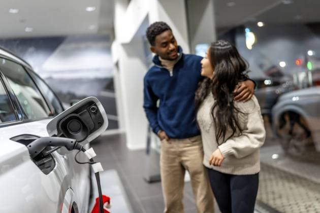 Ein multiethnisches Paar umarmt sich bei der Auswahl eines neuen Elektroautos in einem Autohaus, das sich auf nachhaltige Mobilität konzentriert Multiethnic couple embracing while choosing a new electric car in a dealership, focusing on sustainable transportation Copyright: imageBROKER UnaixHuizi ibxuhu12460355.jpg ,model released, Symbolfoto ,property released