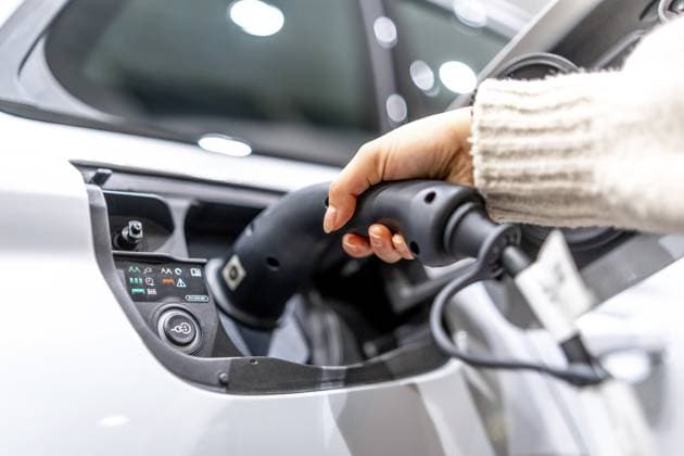 Nahaufnahme einer Hand, die in einem Autohaus ein Ladekabel an ein Elektrofahrzeug anschließt, um den Übergang zu nachhaltigen Verkehrsmitteln zu verdeutlichen Close up of a hand plugging a charging cable into an electric vehicle at a car dealership, showcasing the transition to sustainable transportation Copyright: imageBROKER UnaixHuizi ibxuhu12460362.jpg ,model released, Symbolfoto ,property released