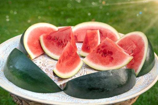 Melons pieces that look like ships lie on an African wooden tray. The melons are standing on green summer meadow with sunshine. 24394623 RECORD DATE NOT STATED