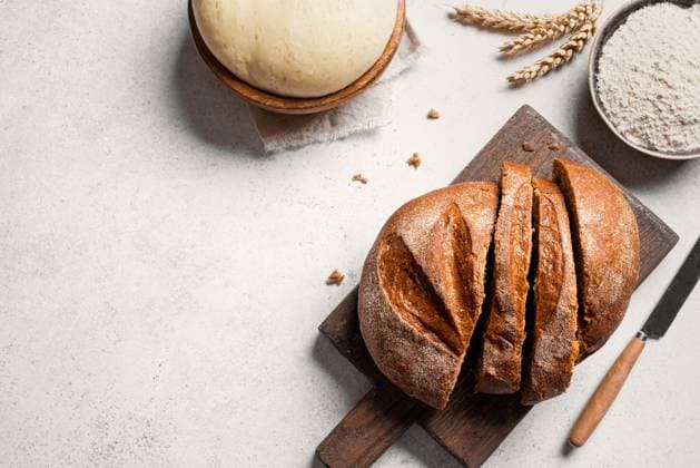 Frisch geschnittenes Brot und Zutaten. Brot backen. Fresh sourdough bread and ingredients. sliced loaf of bread on cutting board, yeast dough and flour on white table, baking background, copy space, top view. Copyright: xZoonar.com OksanaxBratanovax 22882301