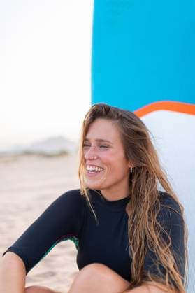 Creative Highlights Symbolfotos MR_GloriaBanuls_PadelSurf.jpg Cheerful female surfer sitting with blue SUP board on sandy seashore in summer and looking away Model Released LeoPastor_ID18063_543450_040 Copyright: xLeoxPastorx